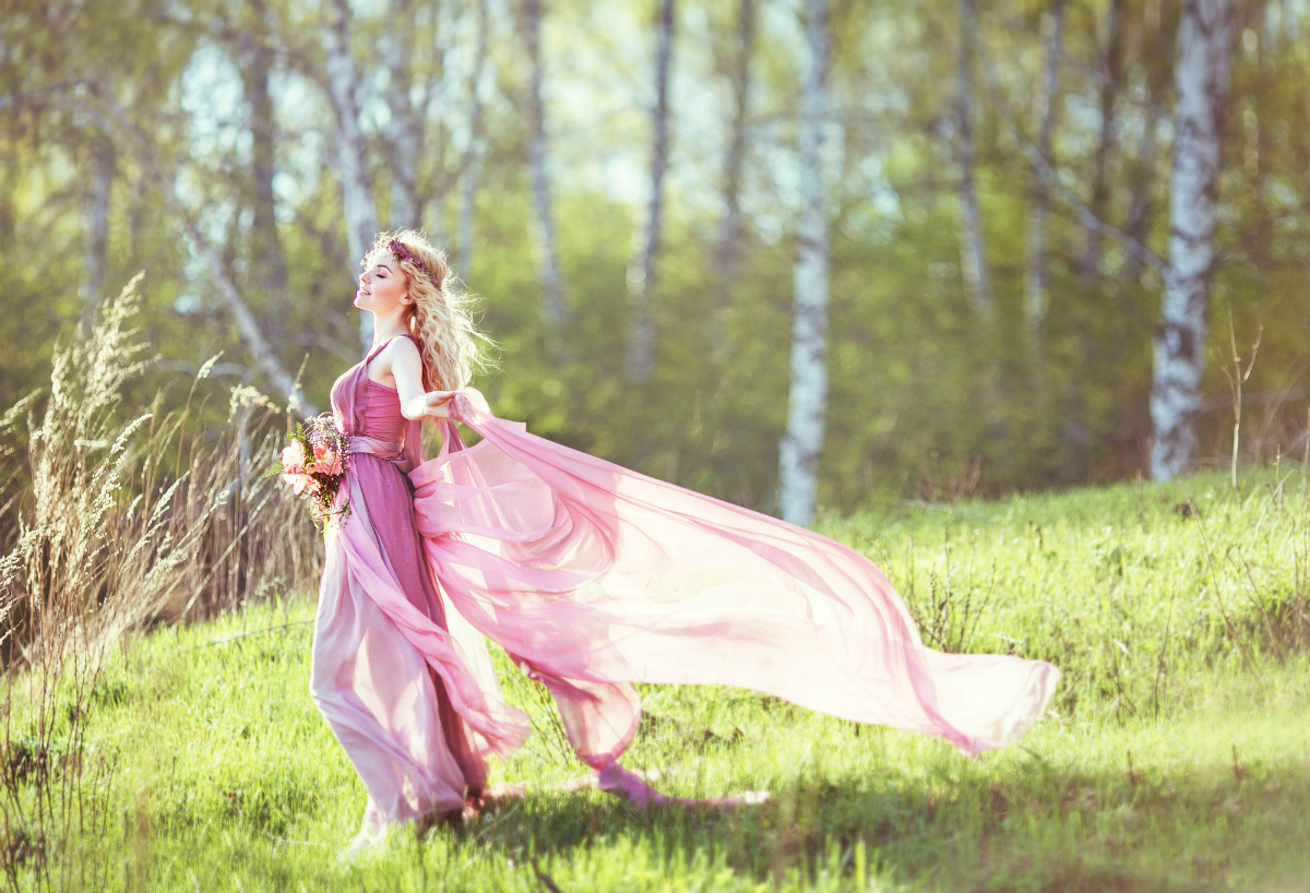 Beautiful blonde girl in a pink dress on a long evolving nature background